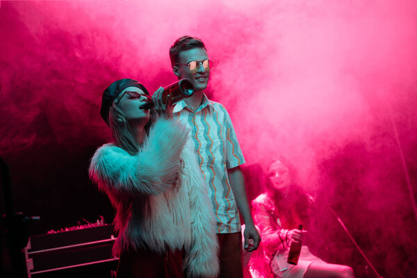 beautiful young woman drinking beer near man in nightclub during rave