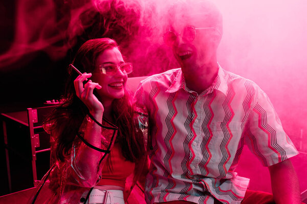 man and young woman with cigarette laughing during rave party in nightclub