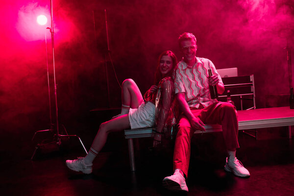 man and young woman sitting together during rave party in nightclub with pink smoke