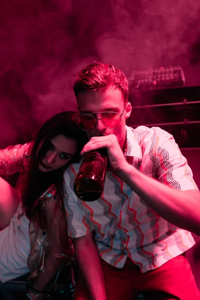 man with beer embracing girl in nightclub during rave