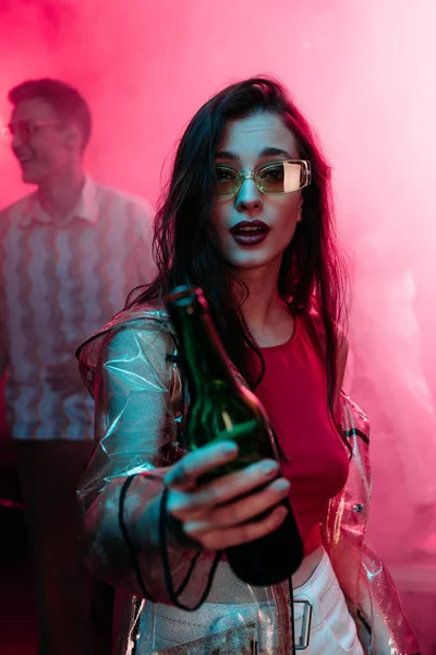 girl in sunglasses with bottle of alcohol during rave in nightclub