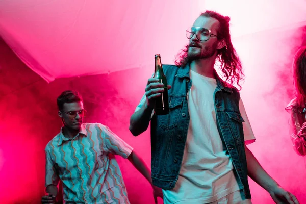 handsome man holding beer in nightclub and dancing during rave