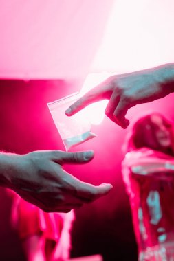 partial view of man passing drugs in plastic zipper bag to man in nightclub clipart