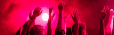 panoramic shot of back view of people with raised hands during rave party in nightclub clipart