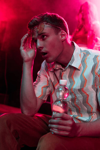 man sitting with bottle of water in nightclub and touching head