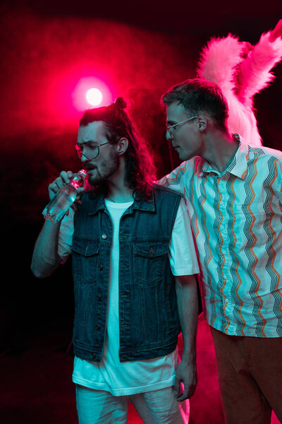 man hugging another man with water bottle in nightclub during rave party 