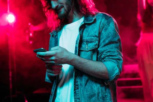 Cropped view of man using smartphone during rave party in nightclub