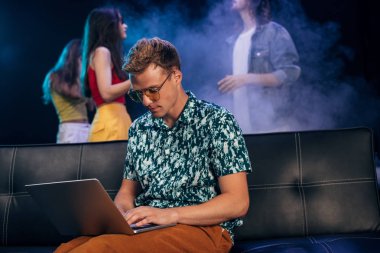 güneş gözlüğü adam kanepede oturan ve gece kulübünde dizüstü bilgisayar kullanarak