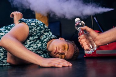 man in sunglasses lying on floor near bottle of water in nightclub clipart