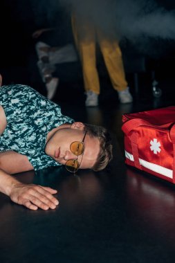 gece kulübünde ilk yardım çantası yakınında yerde yatan güneş gözlüğü adam