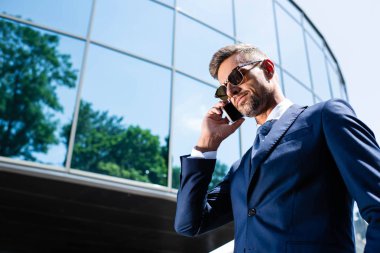 takım elbiseli yakışıklı adamın düşük açılı görünümü ve akıllı telefonda konuşan gözlük 