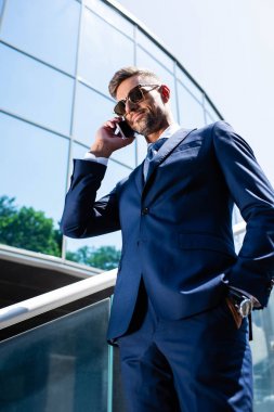 takım elbiseli yakışıklı adamın düşük açılı görünümü ve akıllı telefonda konuşan gözlük 