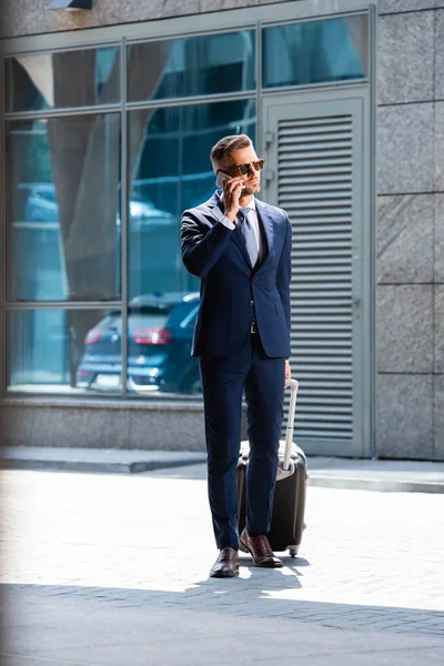 Hombre Guapo Traje Gafas Sosteniendo Maleta Hablando Teléfono Inteligente — Foto de Stock