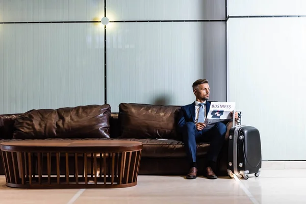 スーツを着たハンサムなビジネスマンがソファに座って新聞を持っている — ストック写真