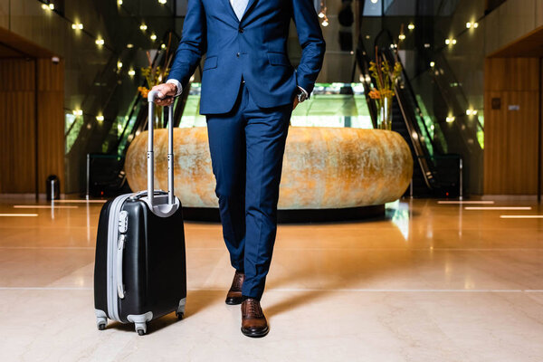 cropped view of businessman in suit with hand in pocket holding suitcase