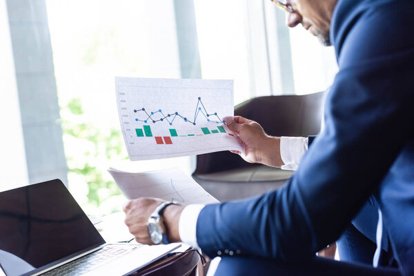 cropped view of man in formal wear looking at papers with charts and graphs