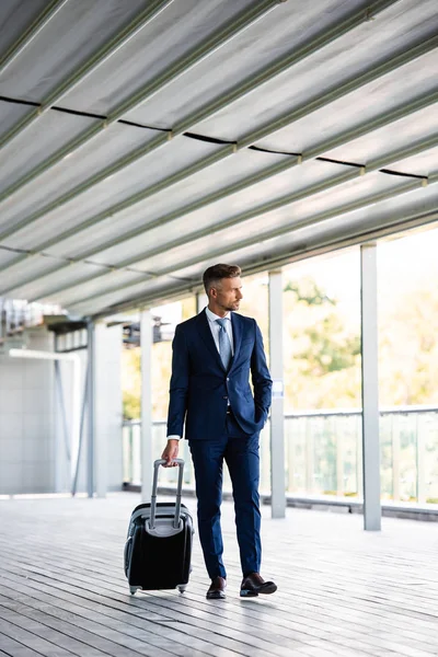 正式な着用スーツケースを持つハンサムで自信のあるビジネスマン — ストック写真