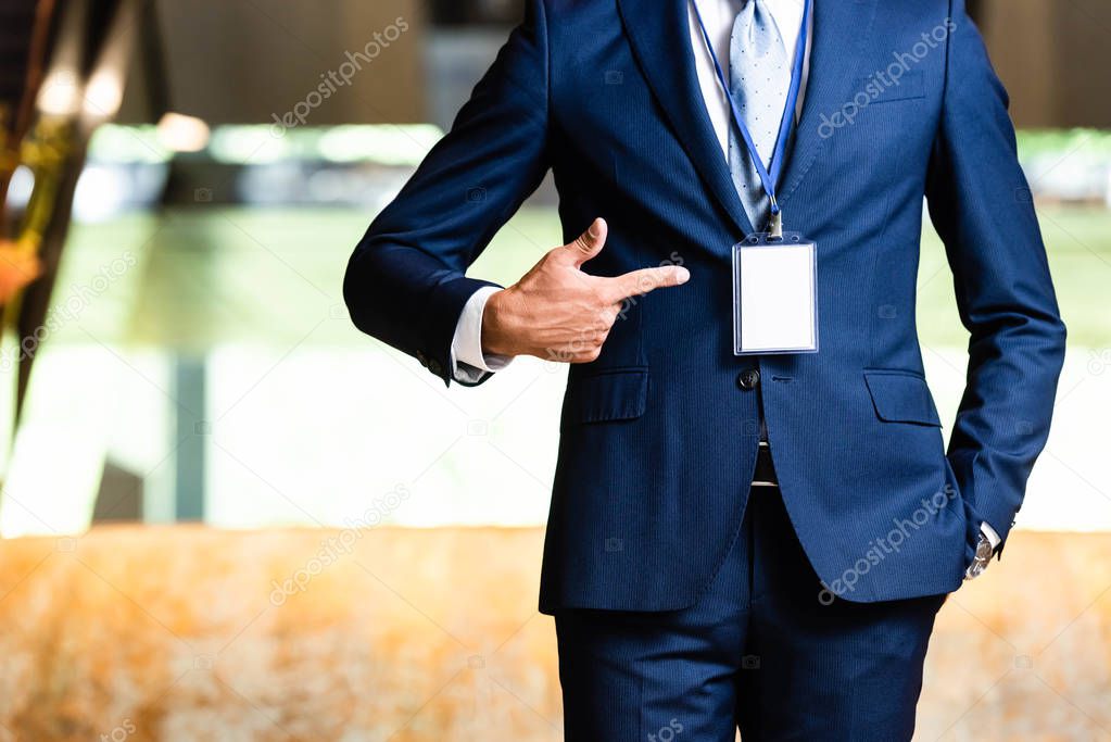 cropped view of man in suit pointing with finger at badge