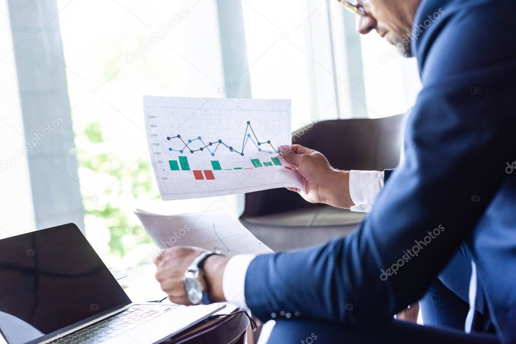 cropped view of man in formal wear looking at papers with charts and graphs