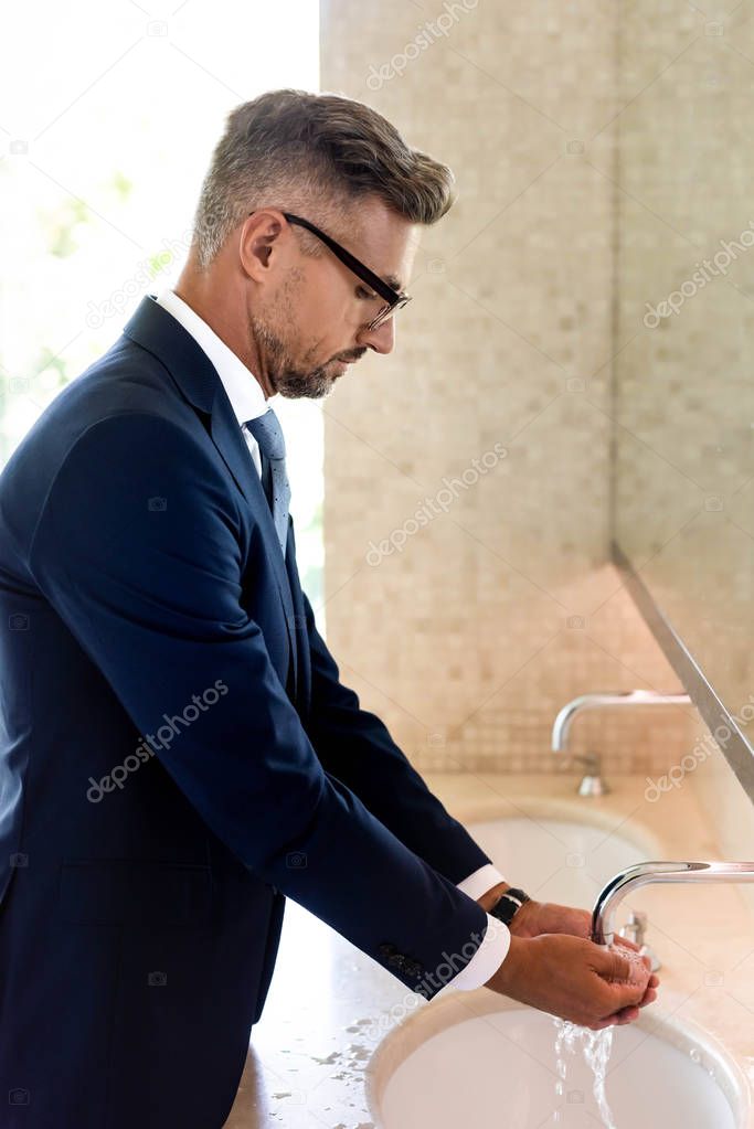 side view of handsome businessman in formal wear and glasses washing hands 