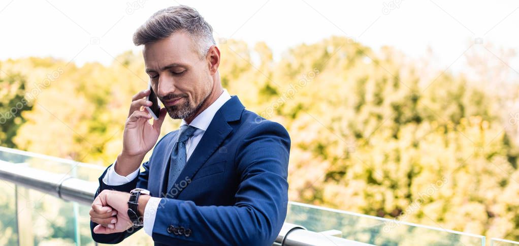 panoramic shot of handsome businessman in formal wear talking on smartphone 