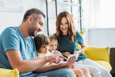 mutlu baba gülümseyen eşi yakın çocuklara akıllı telefon gösterirken parmak ile işaret