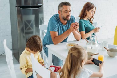 kahvaltı servis ile masada mutfakta otururken kızı ve som akıllı telefonlar kullanarak ebeveynler