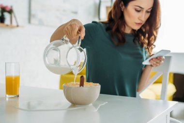 mutfak masasında otururken ve akıllı telefon kullanarak su ile pul kadın overfilling kase