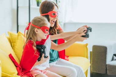 Kiev, Ukrayna - 5 Temmuz 2019: Evde video oyunu oynayan süper kahraman kostümleri heyecanlı anne ve kızı