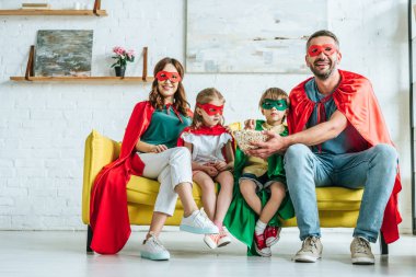 patlamış mısır yeme ve evde tv izlerken süper kahraman kostümleri mutlu aile