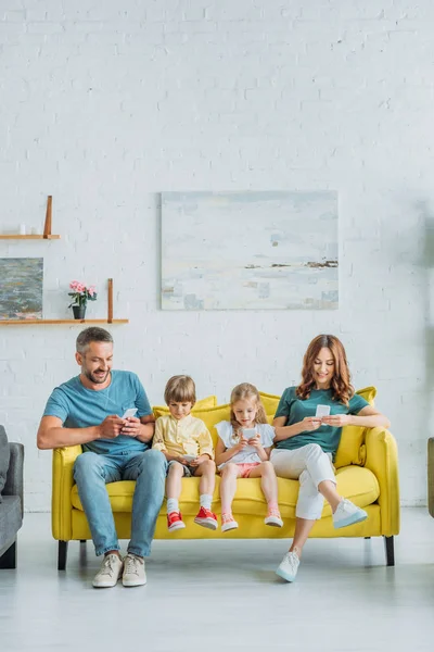 Evde Sarı Kanepede Otururken Akıllı Telefonlar Kullanarak Gülümseyen Aile — Stok fotoğraf