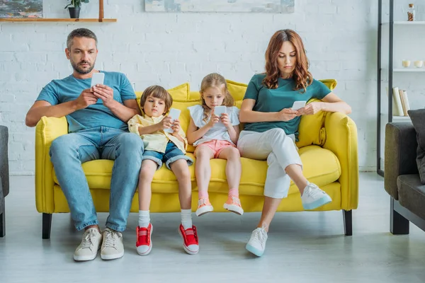 Familia Atenta Sentado Sofá Amarillo Casa Uso Teléfonos Inteligentes —  Fotos de Stock