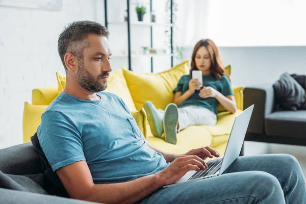 Foco Seletivo Homem Sério Usando Laptop Enquanto Sentado Sofá Perto — Fotografia de Stock