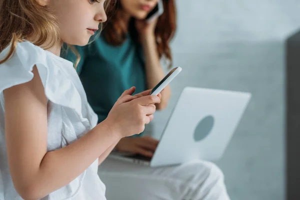 Foco Seletivo Criança Bonita Usando Smartphone Perto Mãe Usando Laptop — Fotografia de Stock
