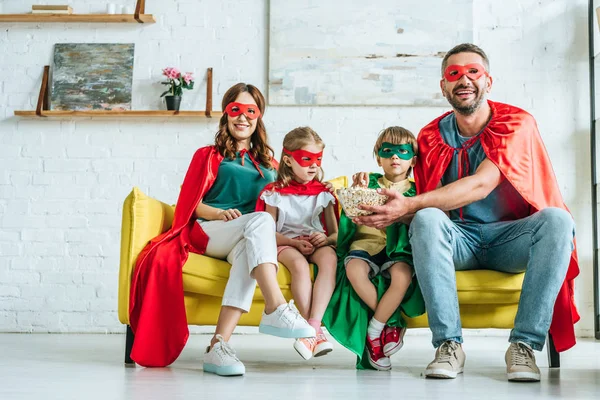 ポップコーンを食べ 自宅でテレビを見ているスーパーヒーローの衣装で幸せな家族 — ストック写真