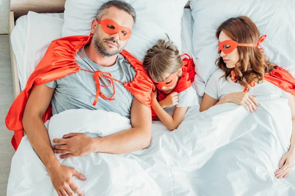 スーパーヒーローの衣装でベッドで眠っているトップビューの父 母と息子 — ストック写真