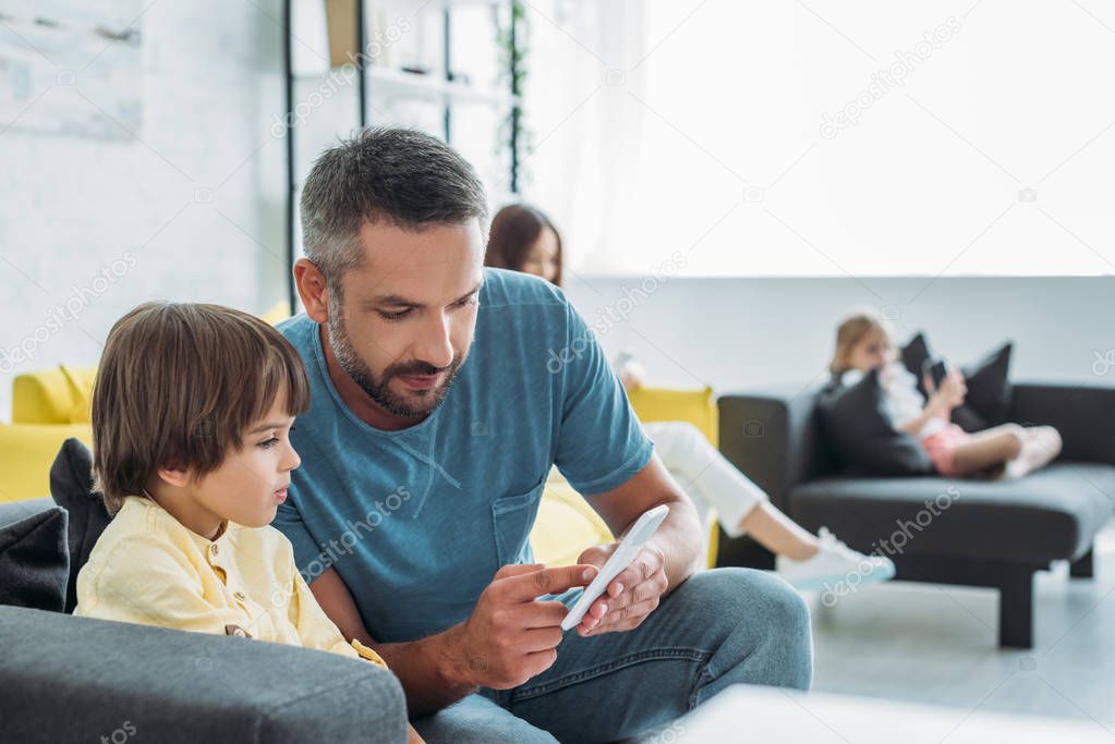 selective focus of father showing smartphone to cute son near mother and daughter using smartphones at home