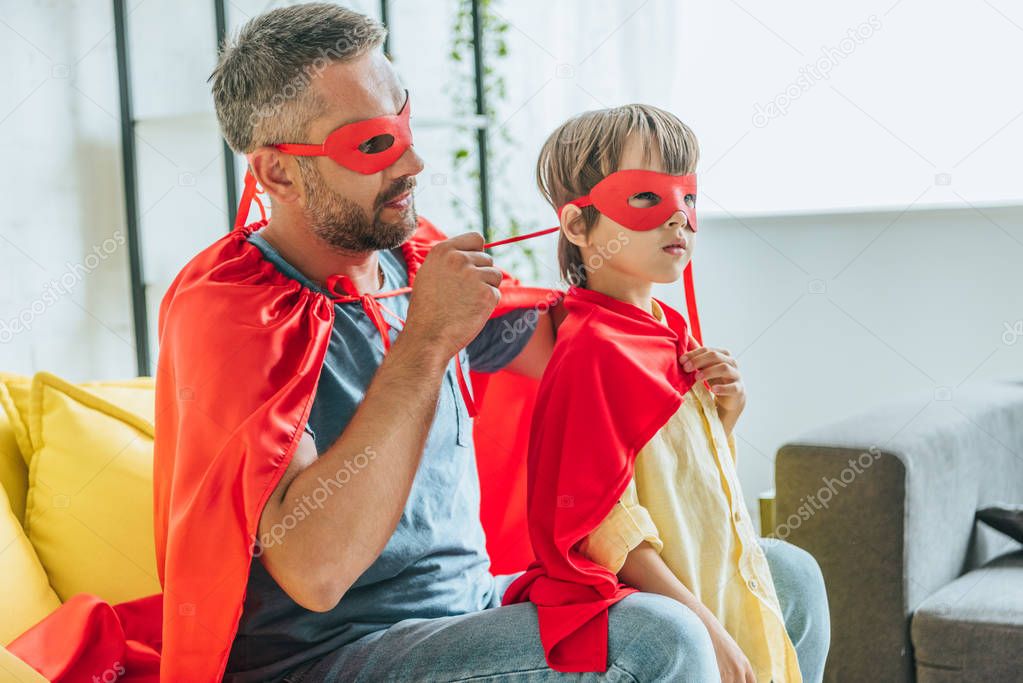 father in costume of superhero putting on red mask on son