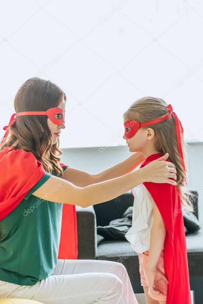 mother and daughter in costumes of superheroes looking at each other at home