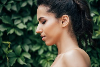 yeşil yaprakların yanında çekici genç ve çıplak kadın yan görünümü