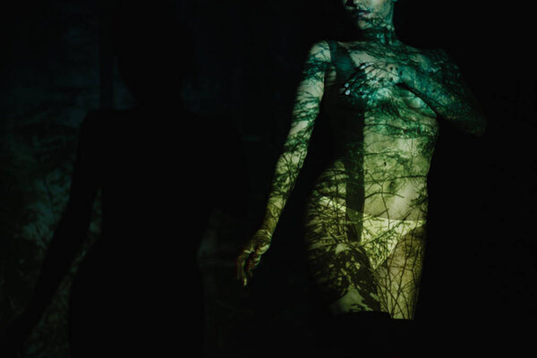 cropped view of undressed young woman with shadows on body standing on black 