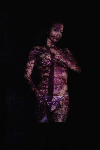 beautiful young woman with shadows on body covering breasts standing on black 