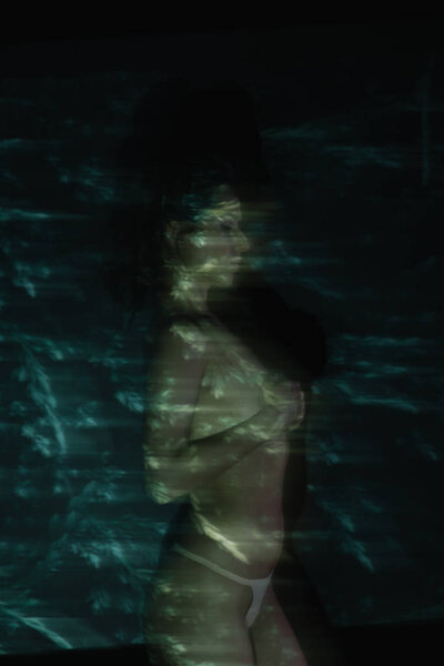 motion blur of girl standing and covering breasts on black 