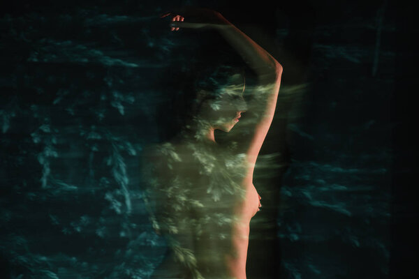 girl standing and covering breasts near fir trees on black 