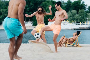 heyecanlı, genç çok kültürlü erkekler plajda futbol oynuyor