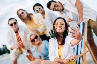 plajda eğlenen çok kültürlü arkadaşlarıyla selfie çeken çekici genç kadının seçici odağı