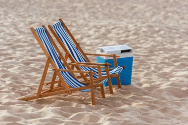 two chaise lounges and cooler box on sunny beach clipart