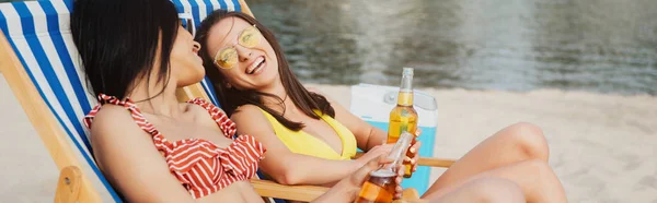 Panoramic Shot Cheerful Beautiful Multicultural Girls Sitting Chaise Lounges Bottles — Stock Photo, Image