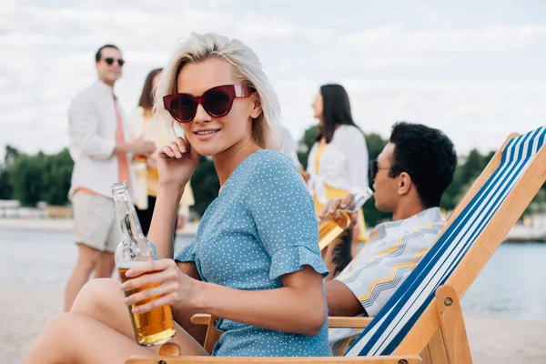 Hermosa Mujer Gafas Sol Sosteniendo Botella Cerveza Mientras Está Sentado — Foto de Stock