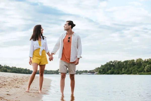 Feliz Pareja Joven Cogidos Mano Mirándose Mientras Caminan Orillas Del — Foto de Stock